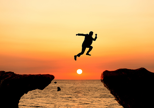 Silhouette of businessman jumping over the cliff.