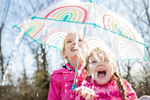 Elementary age sisters go for walk with father and play in the rain with umbrellas