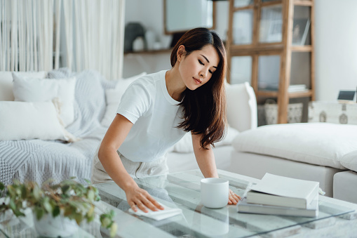 Young Asian woman tidying up the living room and wiping the coffee table surface with a cloth