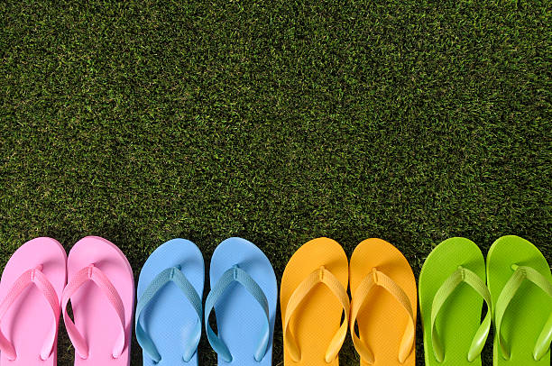 Row of colorful flip flops on grass.