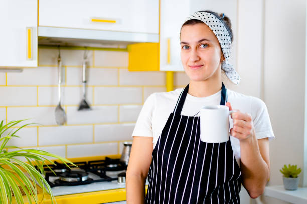 Brunette lady wearing black and white apron making coffee In turk for coffee in kitchen. Concept happy morning leisure.