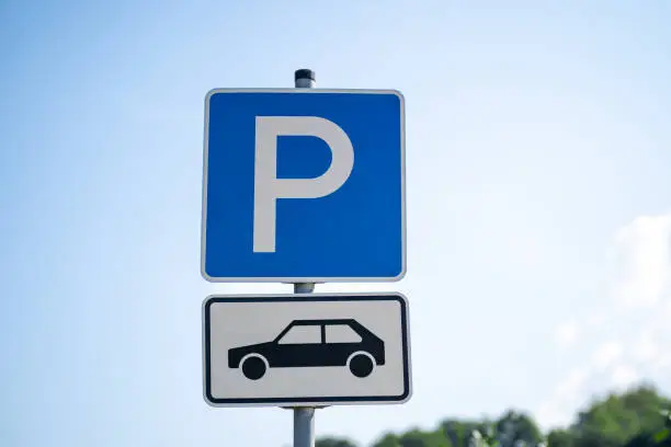 Blue and white parking lot sign with P letter and pictured car in the parking lot. Taken in daytime in summer.