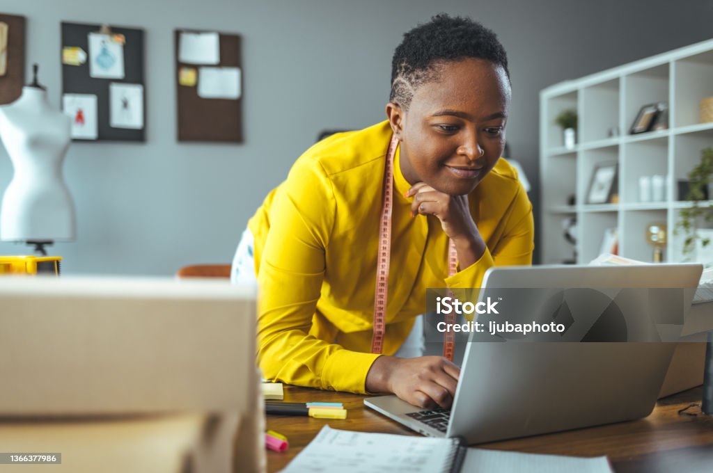 Businesswoman working on laptop in office Female designer working at home office on new ideas. African woman sitting at her desk with laptop reviewing few documents. Office Stock Photo