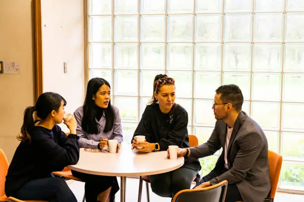 A group of four Asians meet over a cup of coffee at a round table.