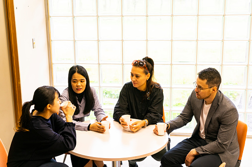 A group of four Asians meet over a cup of coffee at a round table.