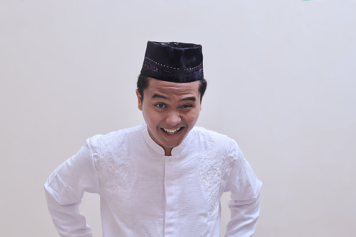 Portrait of religious Asian man in koko shirt or white muslim shirt and black cap with a face of annoyance and anger. Isolated image on gray background