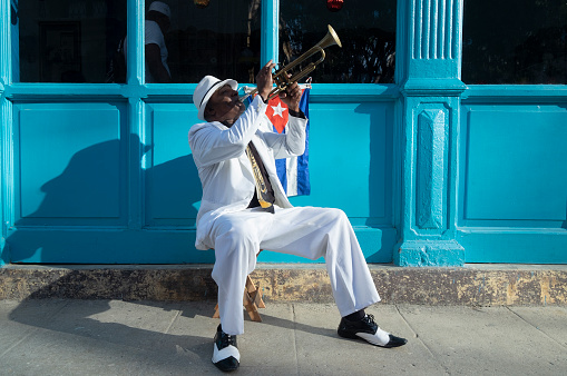 Cuban musician playing the trumpet next to a cuban flag at a street in Old Havana