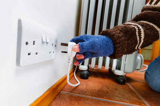Woman with gloved hand plugging in a portable electric heater after the temperature dropped.