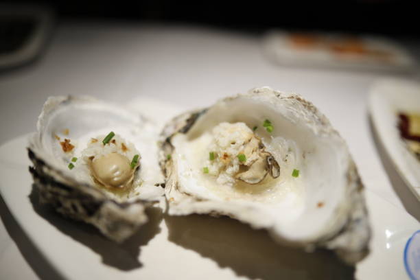 A fresh and appetizing plate of oysters accompanied by lemons, served at an outdoor table. In the background, an Unrecognizable Elegant Woman enjoys a meal, adding to the lively and relaxed dining ambiance