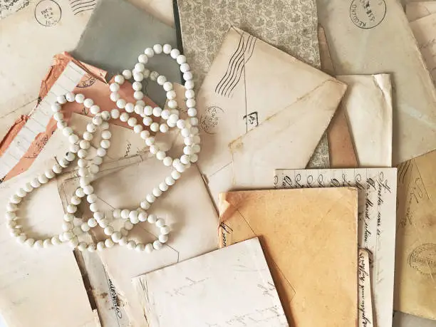 Overhead view of a pearls necklace, over old scattered letters and papers from the beginning of the 20th century.