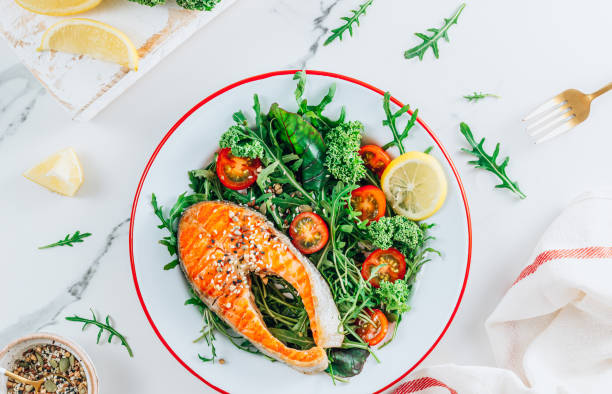 istock Grilled Salmon steak and fresh vegetable salad with a lemon over white marble background. Healty food concept 1366391741
