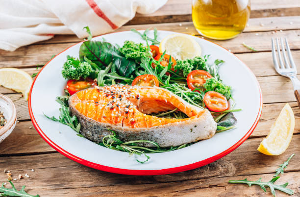 istock Salmon fish steak grilled and fresh vegetable salad on a wooden rustic table. 1366391744