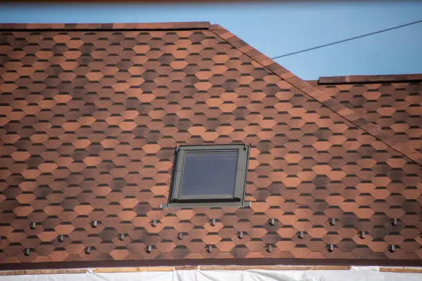 Photo of Roof with mansard windows and shingles. Skylight on a roof shingles under construction