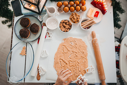 Female sugar baker is decoration christmas cookies with pink icing or frosting, workspace