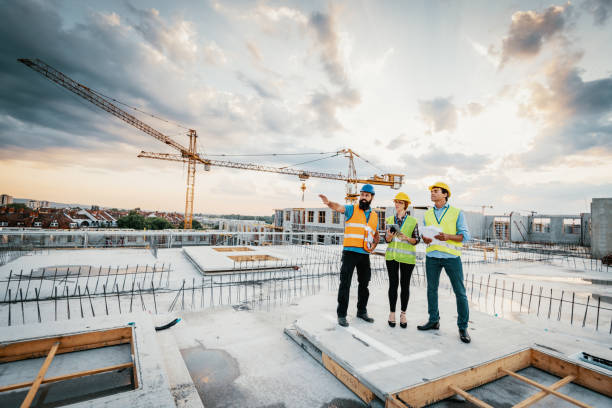 Successful engineers having meeting on construction site Employees working on construction site, wearing protective equipment and discussing next construction phase - full length models visible on the image african american architecture stock pictures, royalty-free photos & images