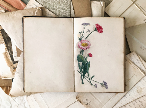 Overhead view of a vintage journal open-wide with watercolor flowers painting,  on top of old scattered letters from the beginning of the 20th century.