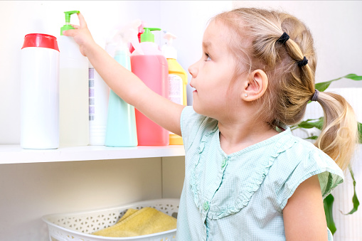 Toddler touches bottles of household chemicals, household cleaning products. Dangerous situation