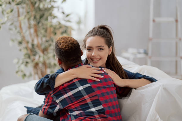 Young students in love, two friends enjoying celebrating happiness sharing joy of buying new apartment hugging reaching out to each other smiling, a beautiful woman with a dark skinned man