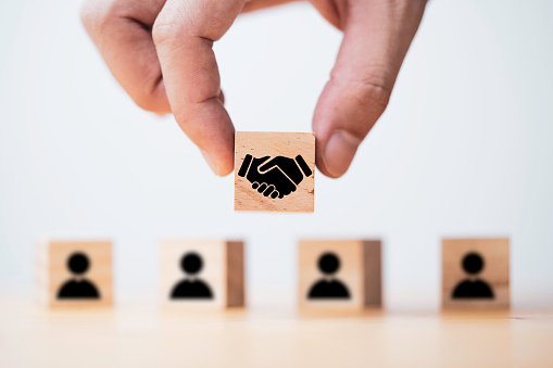 Hand holding wooden cube which drawing of hand shaking print screen on wooden cube block  in front of human icon for business deal and agreement concept.