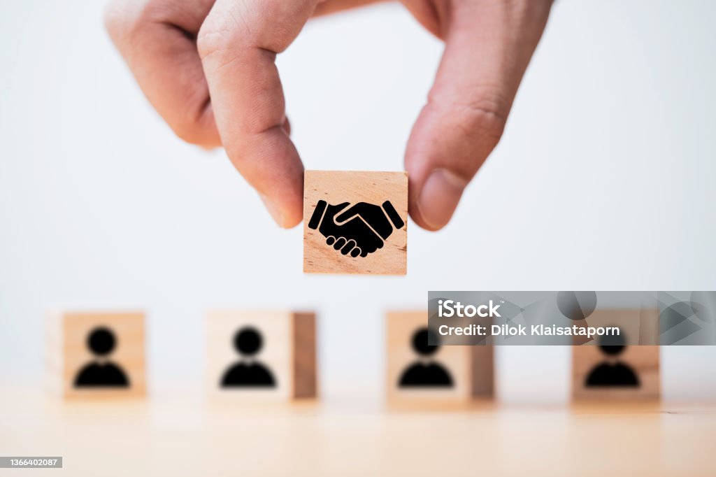 Hand holding wooden cube which drawing of hand shaking print screen on wooden cube block  in front of human icon for business deal and agreement concept. Agreement Stock Photo
