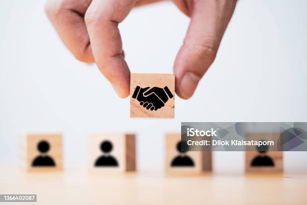 Hand Holding Wooden Cube Which Drawing Of Hand Shaking Print Screen On Wooden Cube Block In Front Of Human Icon For Business Deal And Agreement Concept Stock Photo - Download Image Now