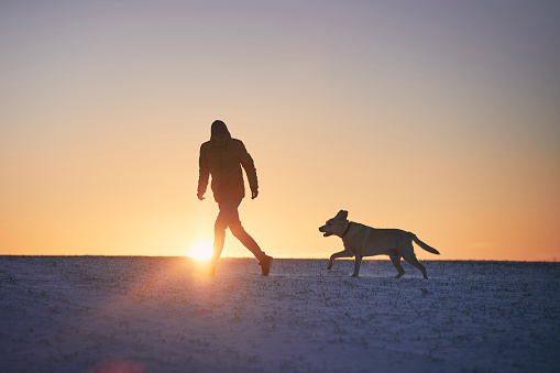 Man with dog running in snow at sunrise