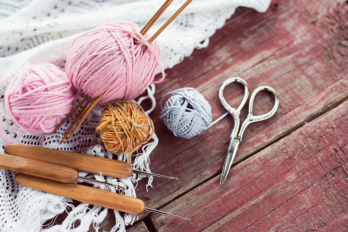 Women's hobby. Crochet and knitting. Working space. Pink skeins of yarn, needles, scissors, crochet hooks on the wood table in the cozy home.