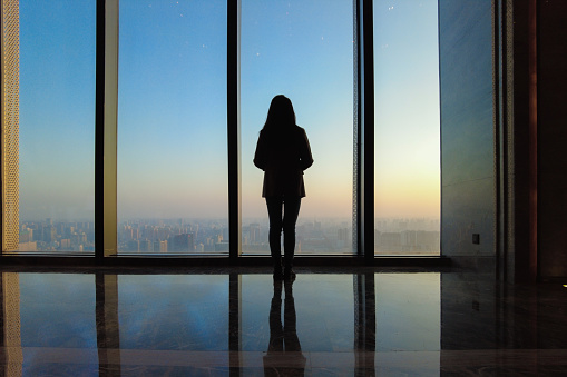 Businesswoman looking through office window at sunset