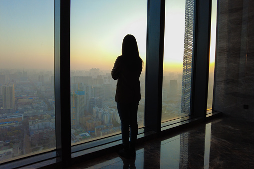 Businesswoman looking through office window at sunset