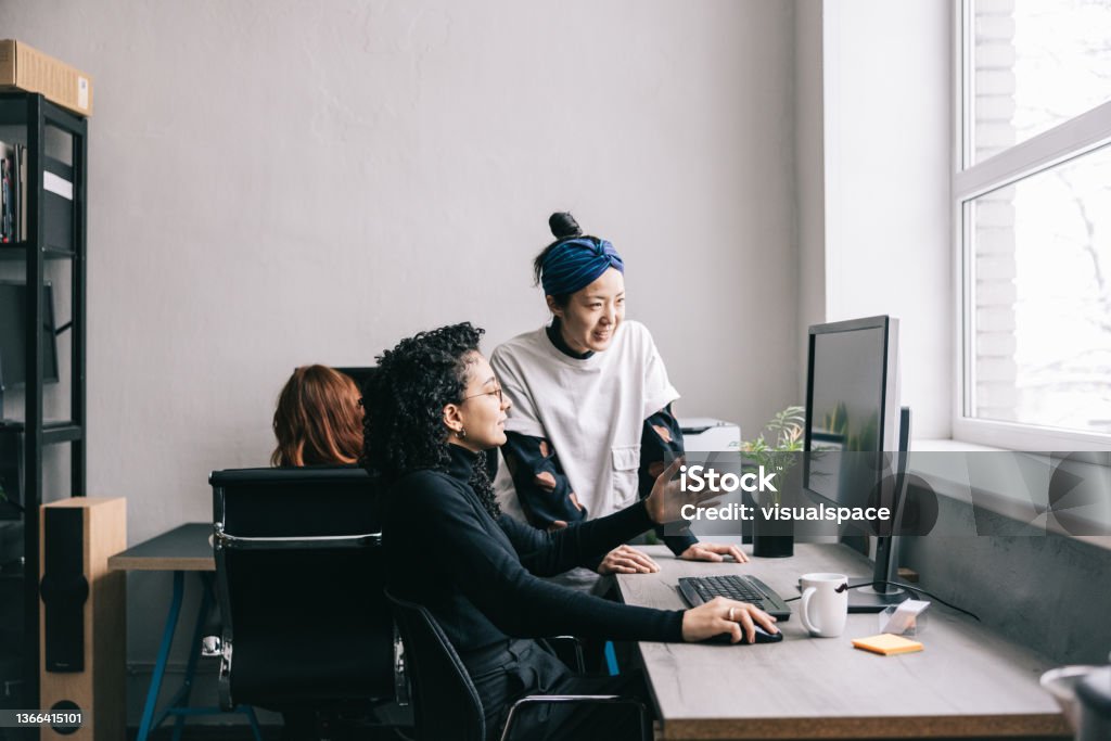 Japanese woman helping her colleague Japanese woman helping her colleague at the office. Computer Programmer Stock Photo