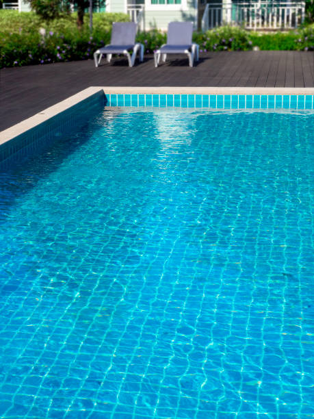 istock Swimming pool with clean clear water, vertical style, nobody. Square shaped pool with blue tiles with sunbeds on the wood decks, no people. water surface. Overhead view.  Summer background. 1366417619