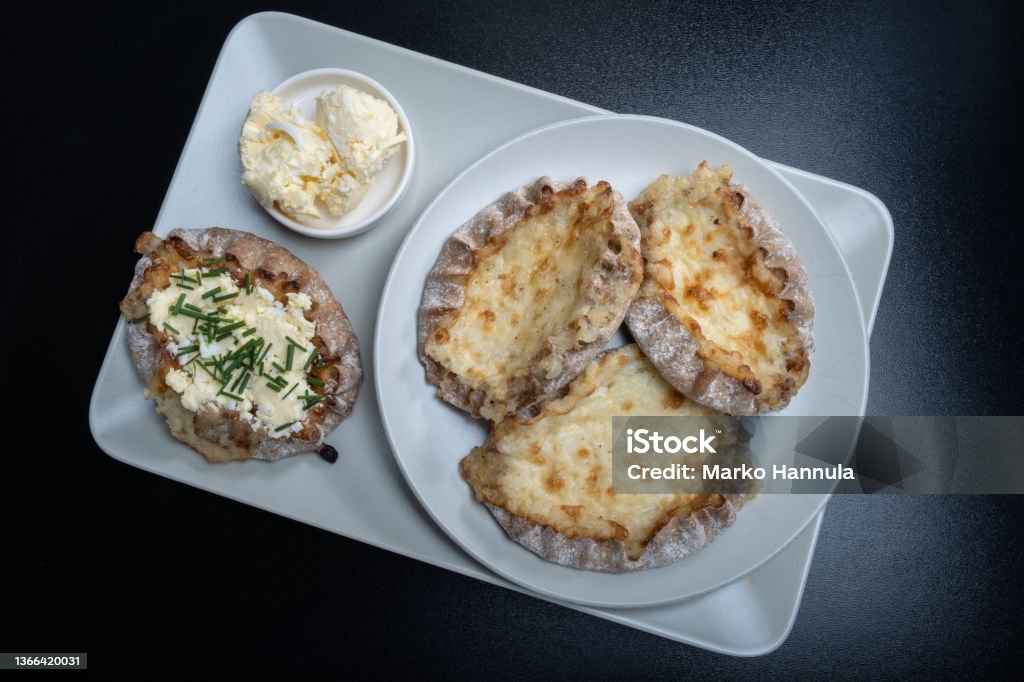 Traditional Finnish foods - Fresh Karelian pies with rice pudding filling and egg butter and chives topping against black background. Helsinki / Finland - JANUARY 21, 2022: Traditional Finnish foods - Fresh Karelian pies with egg butter and chives topping against black background. Finland Stock Photo
