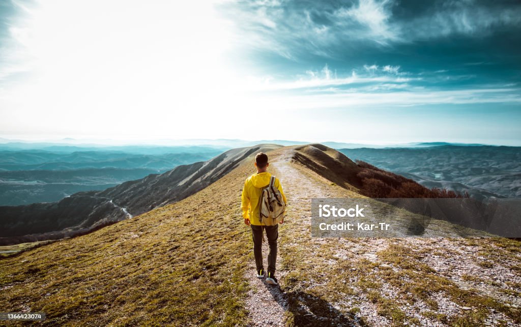 Hiker with backpack hiking on the top of a mountain - Man walking on forest path at sunset - Focus on the guy Travel Stock Photo