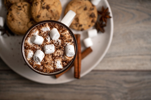 Mug of hot chocolate with marshmallow and cinnamon on a wooden table