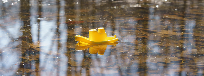 Image of yellow toy boat with natural background. Colorful leaves under water in river. Concepts oe theme of the start up an freedom. Beginning of something new.