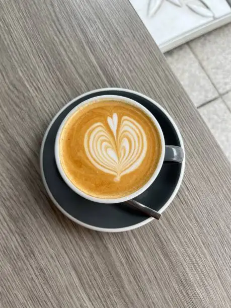 Flatwhite coffee with froth-art in a sea blue cup against wooden backdrop