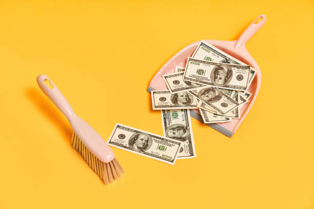 Creative layout with dustpan, hand brooms and money dollar bills on red background. Finance, corruption, criminal activity concept