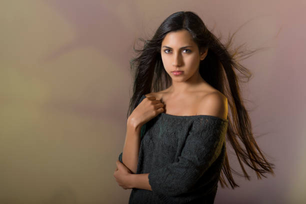 Cold and serious expression of beautiful young girl.She presses one hand to her chest and her hair blows in the wind.