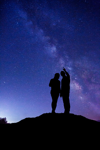 Silhouette of couple holding hands, standing on the mountain looking at the beautiful Milky Way