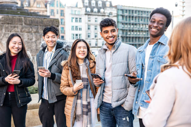 Happy group of friends in the city using mobile phones and laughing together stock photo
