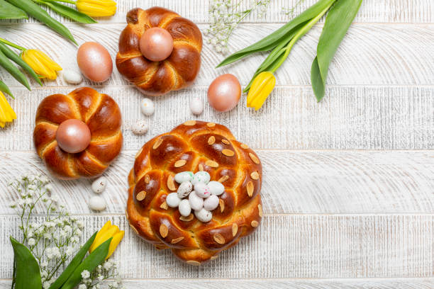 easter background with italian style braid bread and pink metallic  colored eggs, candies. homemade pastry. yellow tulips. white wooden background. top view, copy space. - paastaart stockfoto's en -beelden