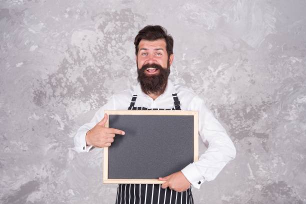 istock cheerful hospitable restaurant waiter with chalkboard, copy space. best choice. advertisement and food. cooking by recipe. Master class from cook man. best offer for dinner. chef baker menu 1366446317