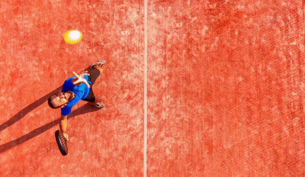 Top view of a professional paddle tennis player who is going to hit the ball during a padel match. The ball is very close to the camera.