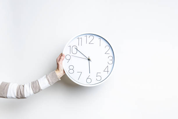 istock Woman's hand holds a large white clock against a light wall. 1366454253