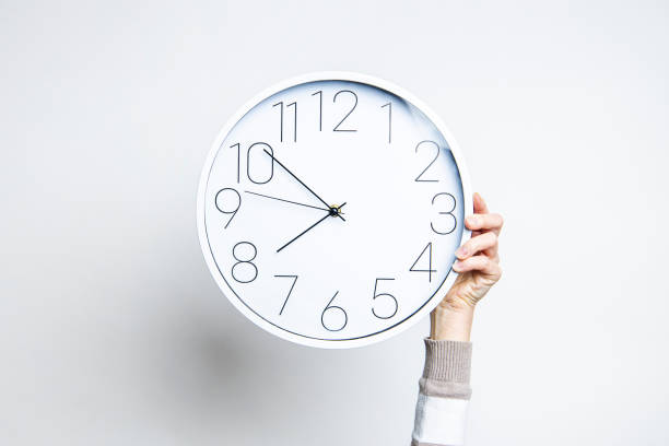 istock Woman's hand holds a large white clock on a light background. 1366454267