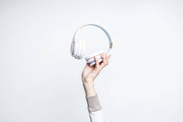 istock Woman's hand holding large white headphones on a light background. 1366454332
