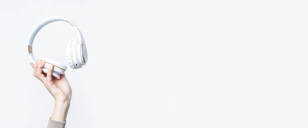istock Woman's hand holding large white headphones on a light background. Banner. 1366454361
