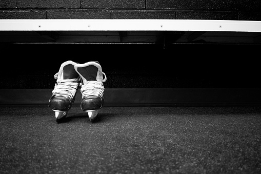 Hockey skates below bench in locker room in black and white with copy space