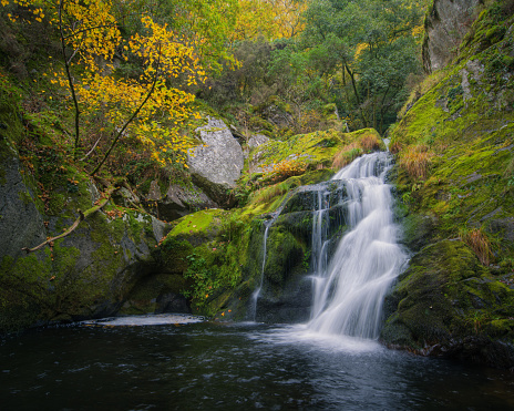 Small waterfall over a pool between granite rocks and autumn forest