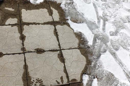 Melting snow on the paving slabs during spring thaw. Patch of sidewalk in thawing snow.